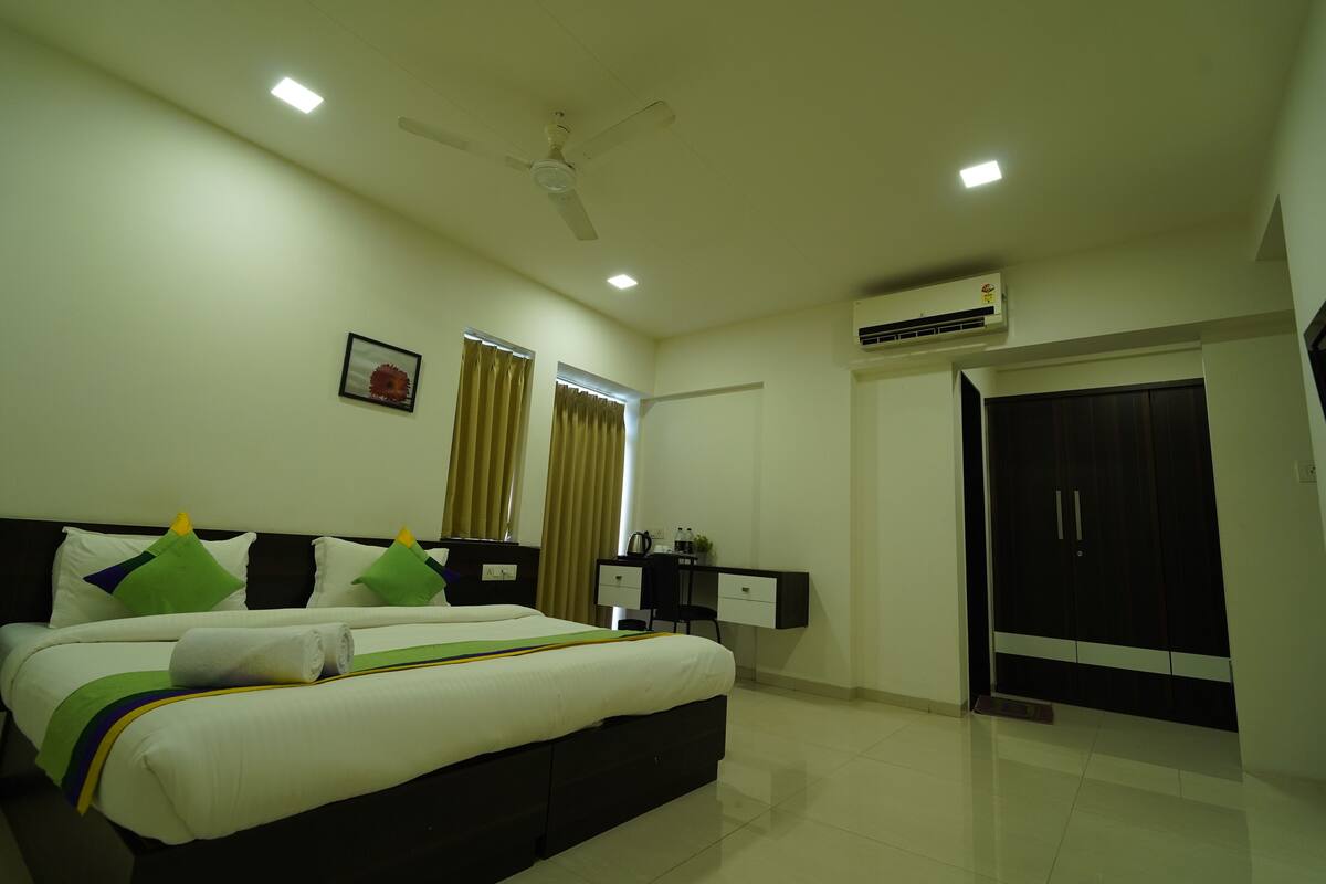 Quarto de hotel com cama, escrivaninha, cadeira, guarda-roupa e ventoinha no teto.