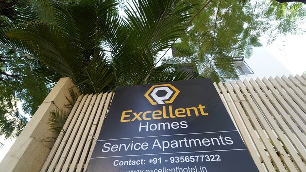 A sign for Excellent Homes Service Apartments with contact information and website URL. - EXCELLENT HOMES (Nashik)