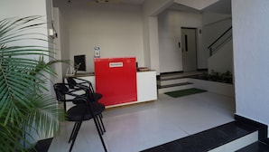 A reception area with a red desk, black chairs, a ceiling fan, and a staircase leading to an upper level. - EXCELLENT HOMES (Nashik)