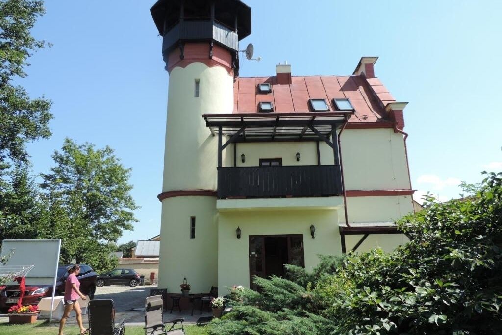 A two-story building with a tower, a balcony, and a small garden area.