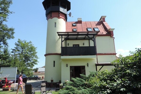 A two-story building with a tower, a balcony, and a small garden area.