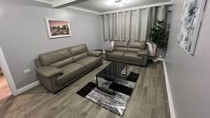 A modern living room with a sectional sofa, a coffee table, and a large window with curtains. - Spacious 3 Bed Home - Ideal for Families & Groups (Linford)