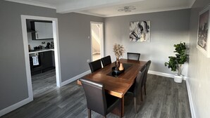 A dining area with a wooden table and chairs, a ceiling fan, and a view into the kitchen. - Spacious 3 Bed Home - Ideal for Families & Groups (Linford)