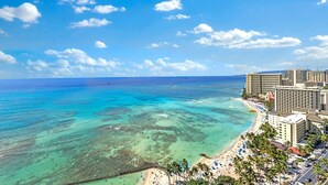 Un hotel frente al mar con vistas a la playa, varios edificios altos y un cielo azul despejado.