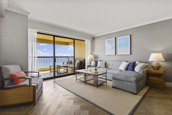 A modern living room with a grey sofa, a wooden coffee table, and a balcony with a view of the sky. - Luxury Oceanfront High Floor @ Waikiki Beach Tower (Honolulu)