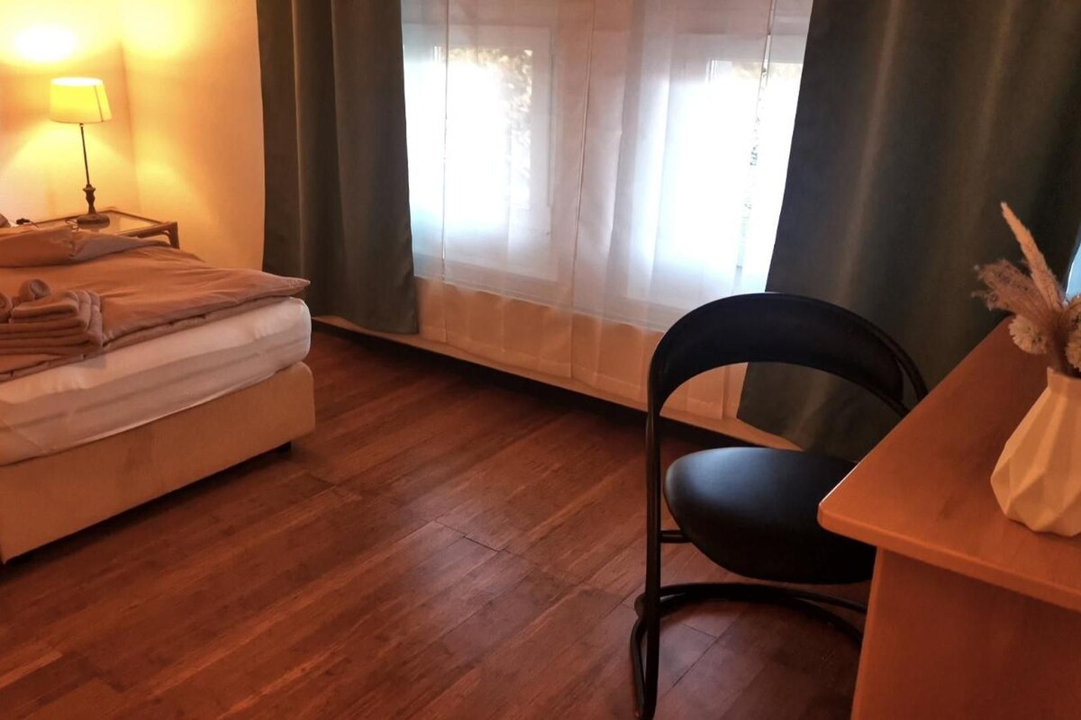 A hotel room with a bed, a chair, a desk, a lamp, and a window with curtains.