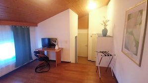 A room with a wooden desk, a chair, a TV, a door, a coat rack, and a framed picture on the wall. - il Fiore - Hotel Ristorante Pizzeria (Steinach)