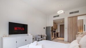 A modern hotel room with a large flat-screen TV, a dining area, a kitchenette, and a separate living space. - LUX Dubai Hills Sway Studio (Dubai)