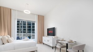 A modern hotel room with a bed, a small dining table with chairs, a TV, and a window with curtains. - LUX Dubai Hills Sway Studio (Dubai)