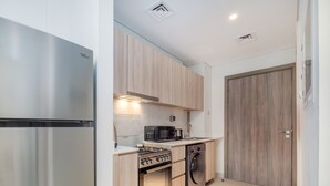 A compact kitchen with a stainless steel refrigerator, a microwave, a gas stove, and a built-in oven. - LUX Dubai Hills Sway Studio (Dubai)