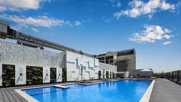 A modern pool area with a clear blue pool, white geometric wall design, and a wooden deck. - LUX Dubai Hills Sway Studio (Dubai)