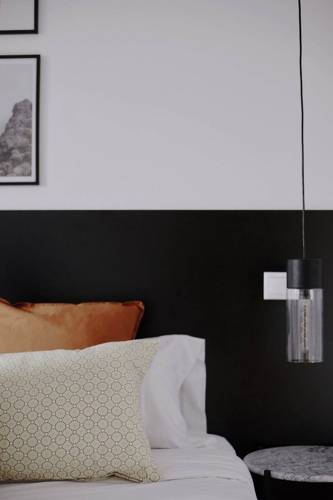 A hotel room with a bed, a pillow, a bedside table, and a hanging light fixture.
