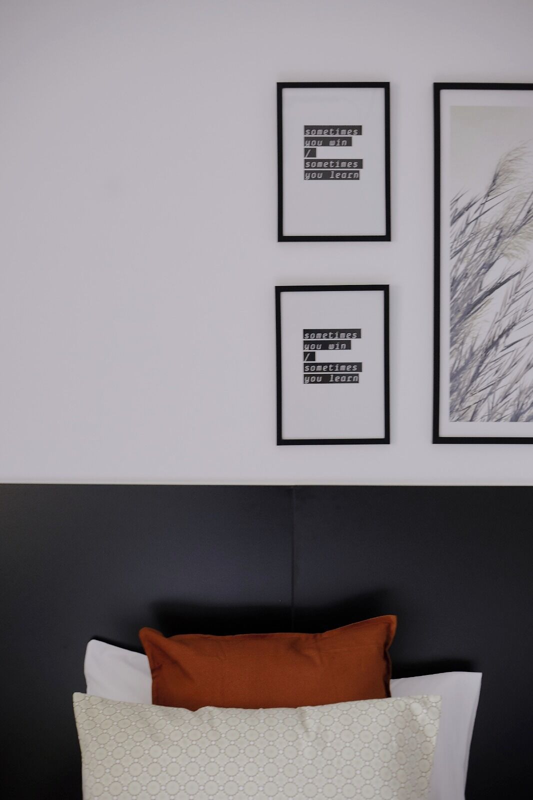 A bedroom with a black headboard, a bed with white and patterned pillows, and two framed motivational quotes on the wall.