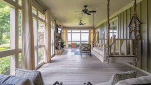 A covered porch with a wooden floor, stone wall, and a view of the outdoors.