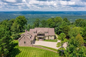 A large, two-story house with a stone facade and a spacious front yard, surrounded by dense forest and a view of distant hills. - French Quarter - New Orleans Charm in the Mountain (Mentone)