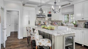 A spacious kitchen with white cabinetry, a marble countertop, and a central island with bar stools.