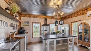 A kitchen with wooden walls, a central island, stainless steel appliances, and a hanging pot rack. - The Prairie House Retreat, Hot Tub, Family ! (Valley Head)