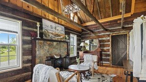 A rustic cabin interior with wooden walls, a stone fireplace, a round wooden table, and a cozy seating area. - The Prairie House Retreat, Hot Tub, Family ! (Valley Head)