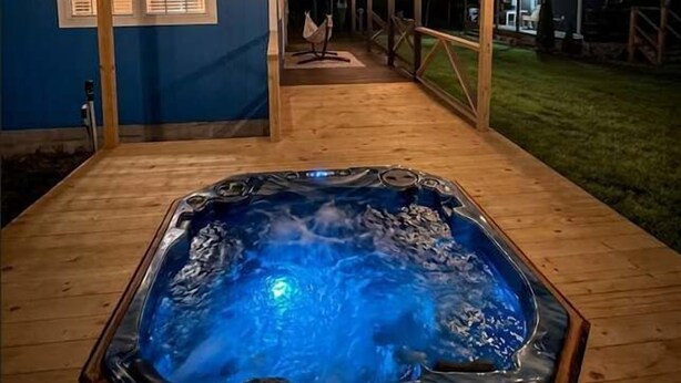 A wooden deck with a hot tub, a covered area with string lights, and a building with blue walls and windows. - The Prairie House Retreat, Hot Tub, Family ! (Valley Head)