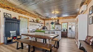 A rustic kitchen with wooden cabinets, a central island, and a dining area with benches. - The Prairie House Retreat, Hot Tub, Family ! (Valley Head)