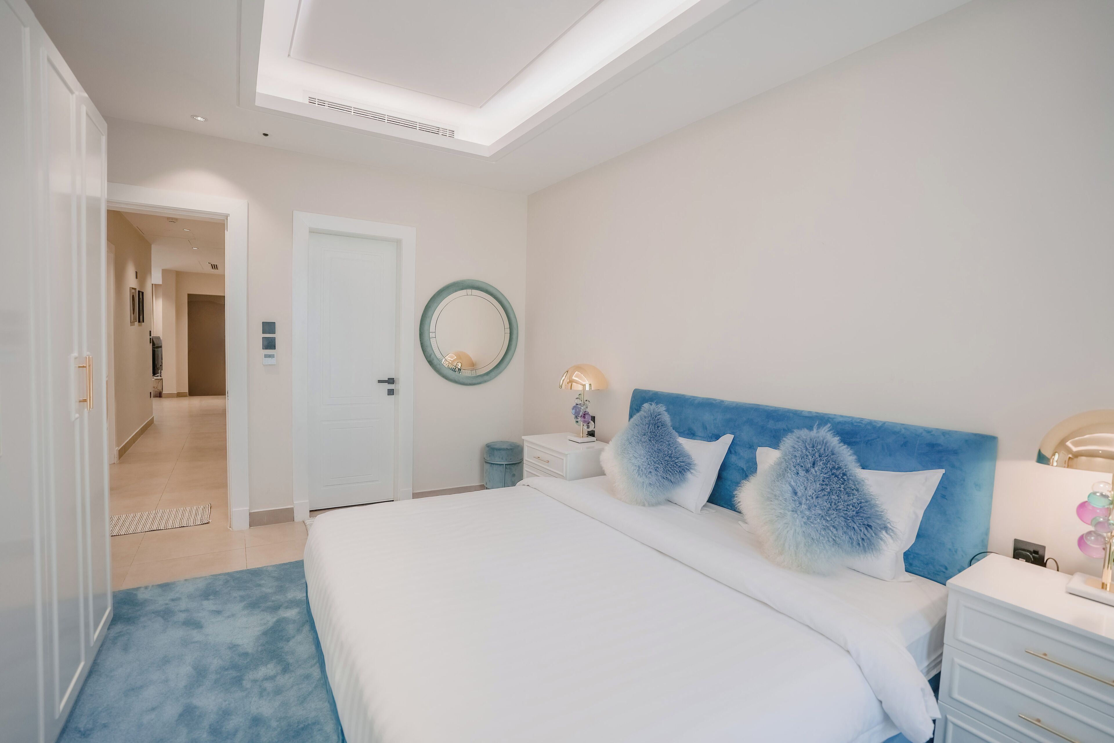 A bedroom with a large bed, a nightstand, a dresser, a mirror, and a door leading to another room.