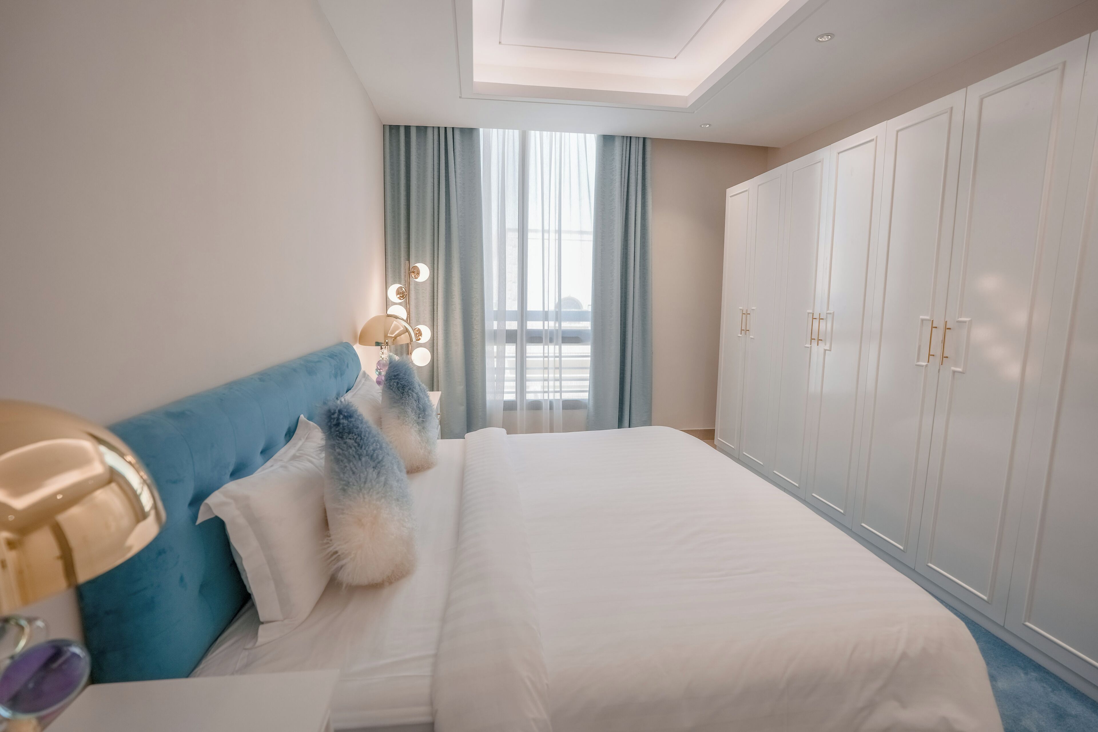 A modern hotel room with a large bed, a vanity with mirrors, and a wardrobe.