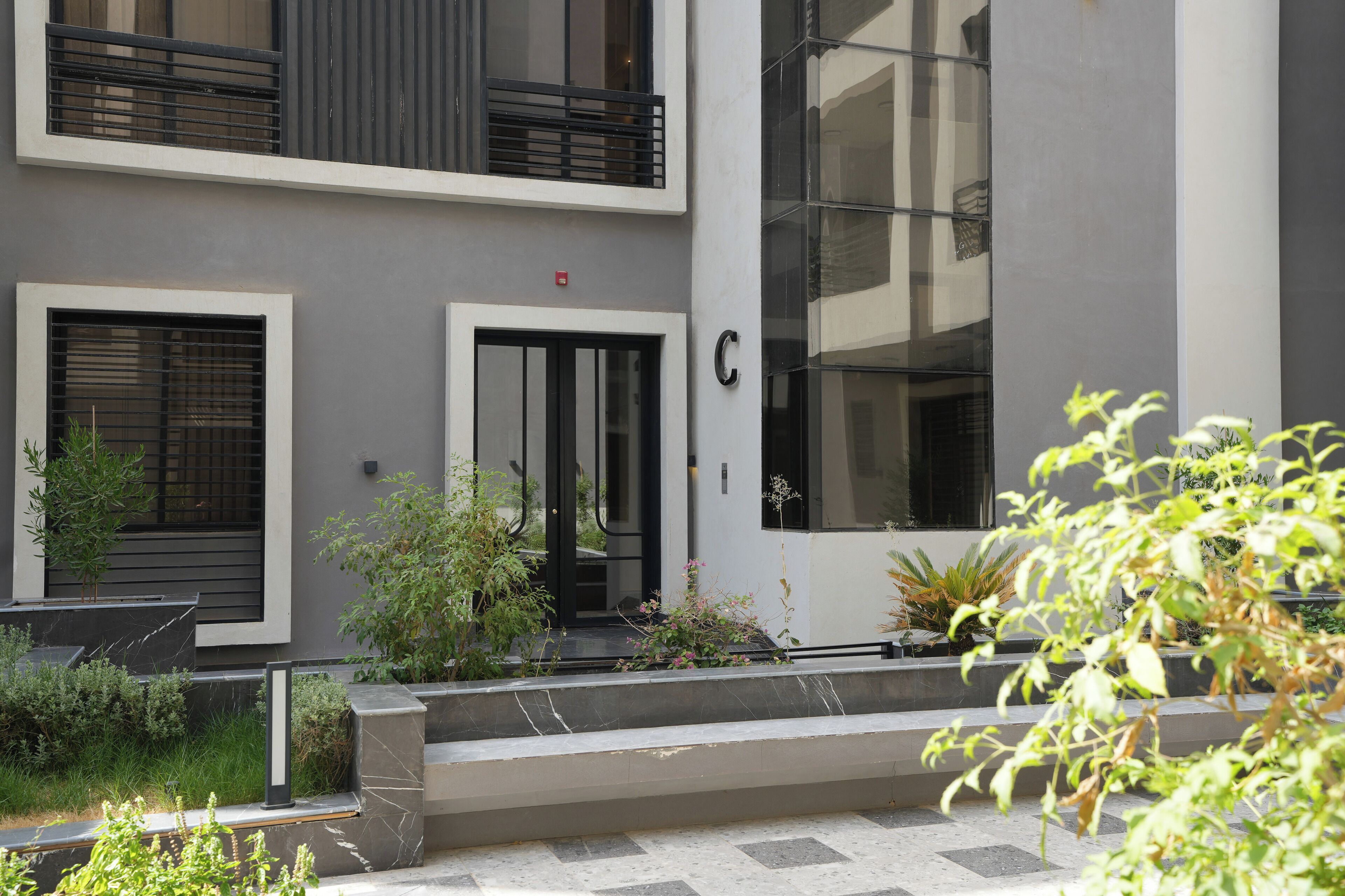 A modern building with a grey facade, a large window, and a door marked with a 'C'.