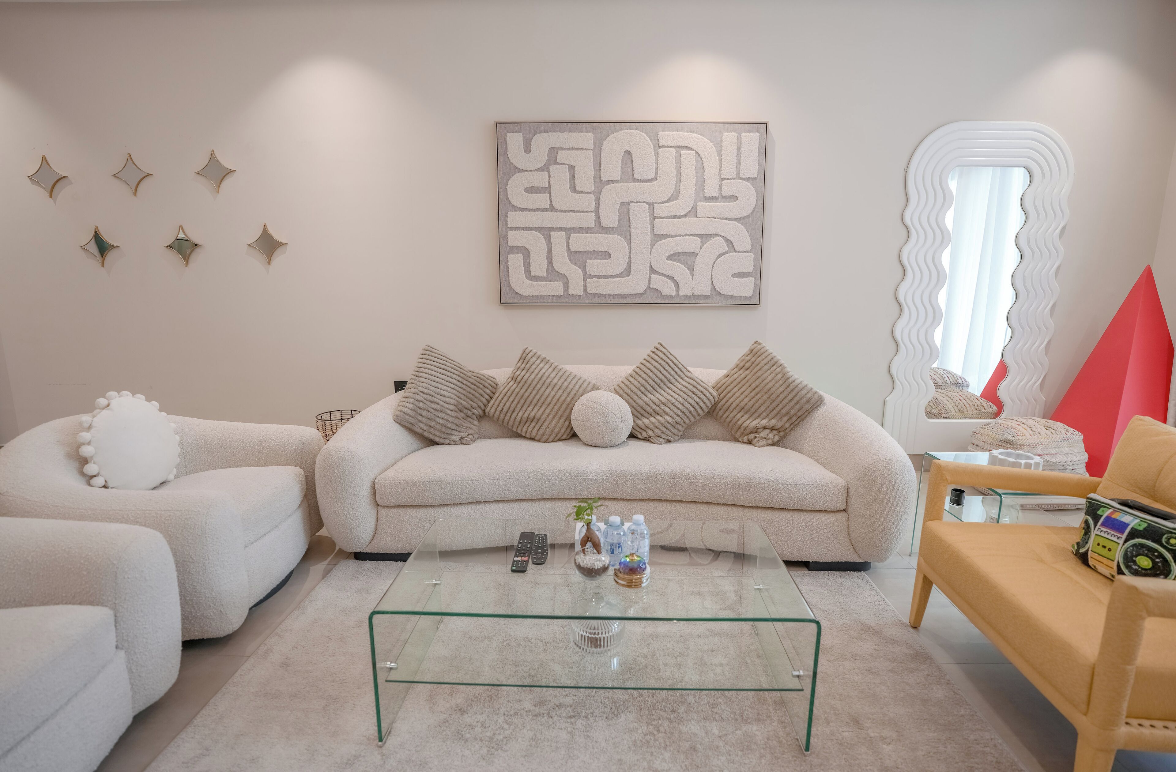 A modern living room with a beige sofa, a glass coffee table, and a red accent chair.