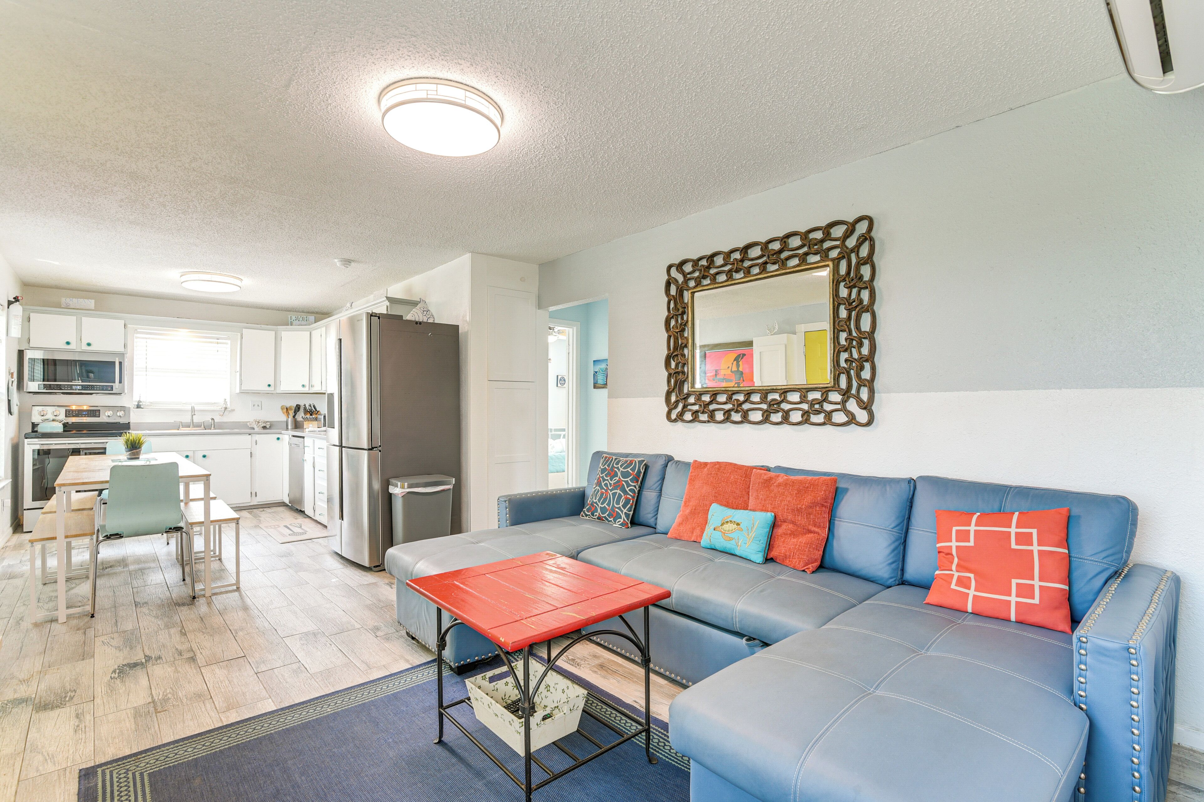 A modern living room with a blue sofa, red coffee table, and a kitchen in the background.