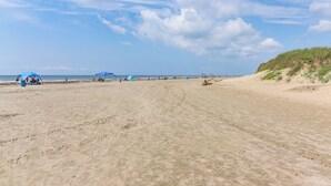 A sandy beach with blue umbrellas and a dune on the right.