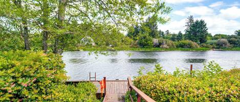 A wooden deck leading to a calm lake surrounded by lush greenery and trees.