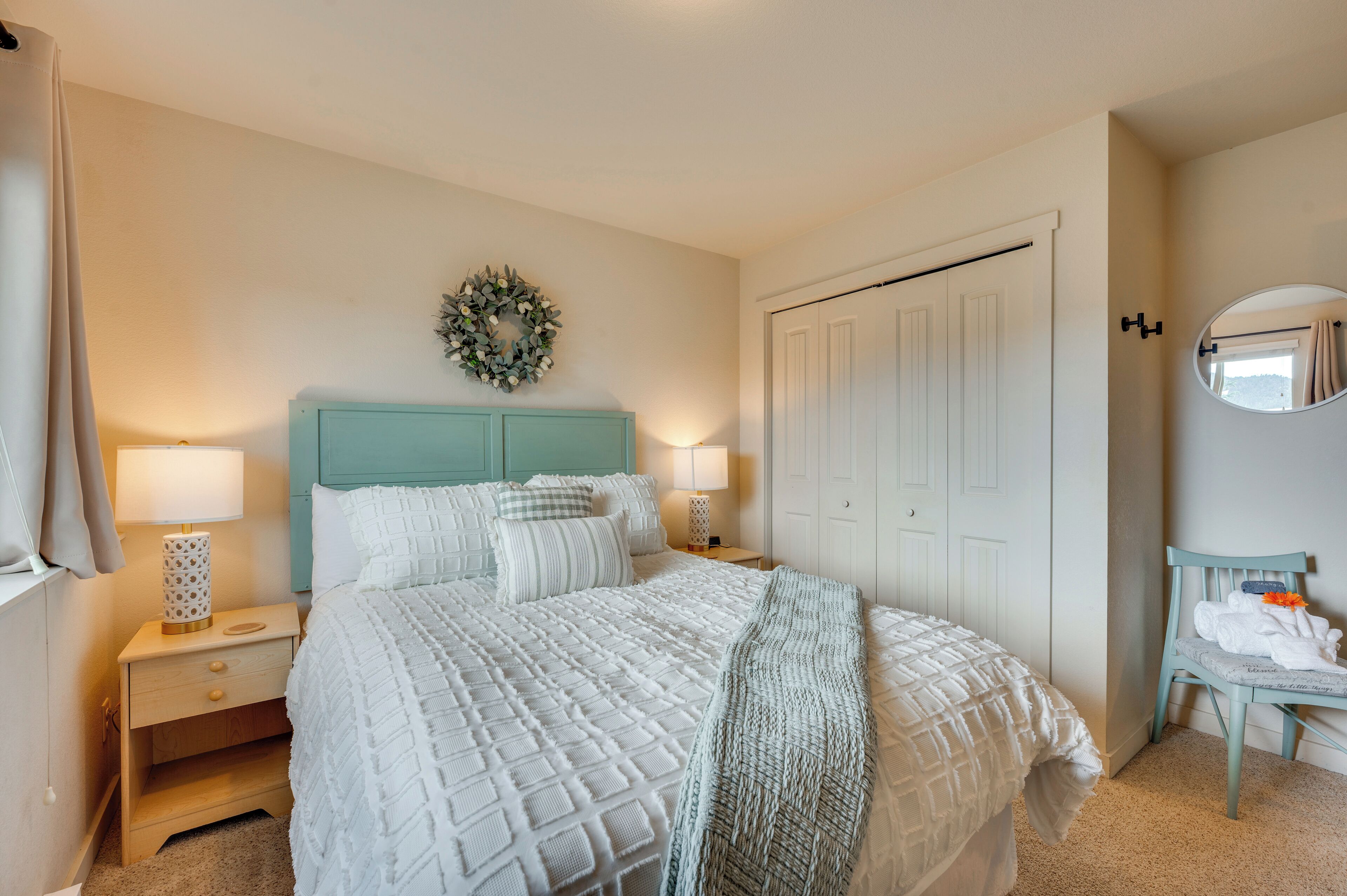 Un dormitorio con cama, mesitas de noche, cómoda, espejo y una puerta.