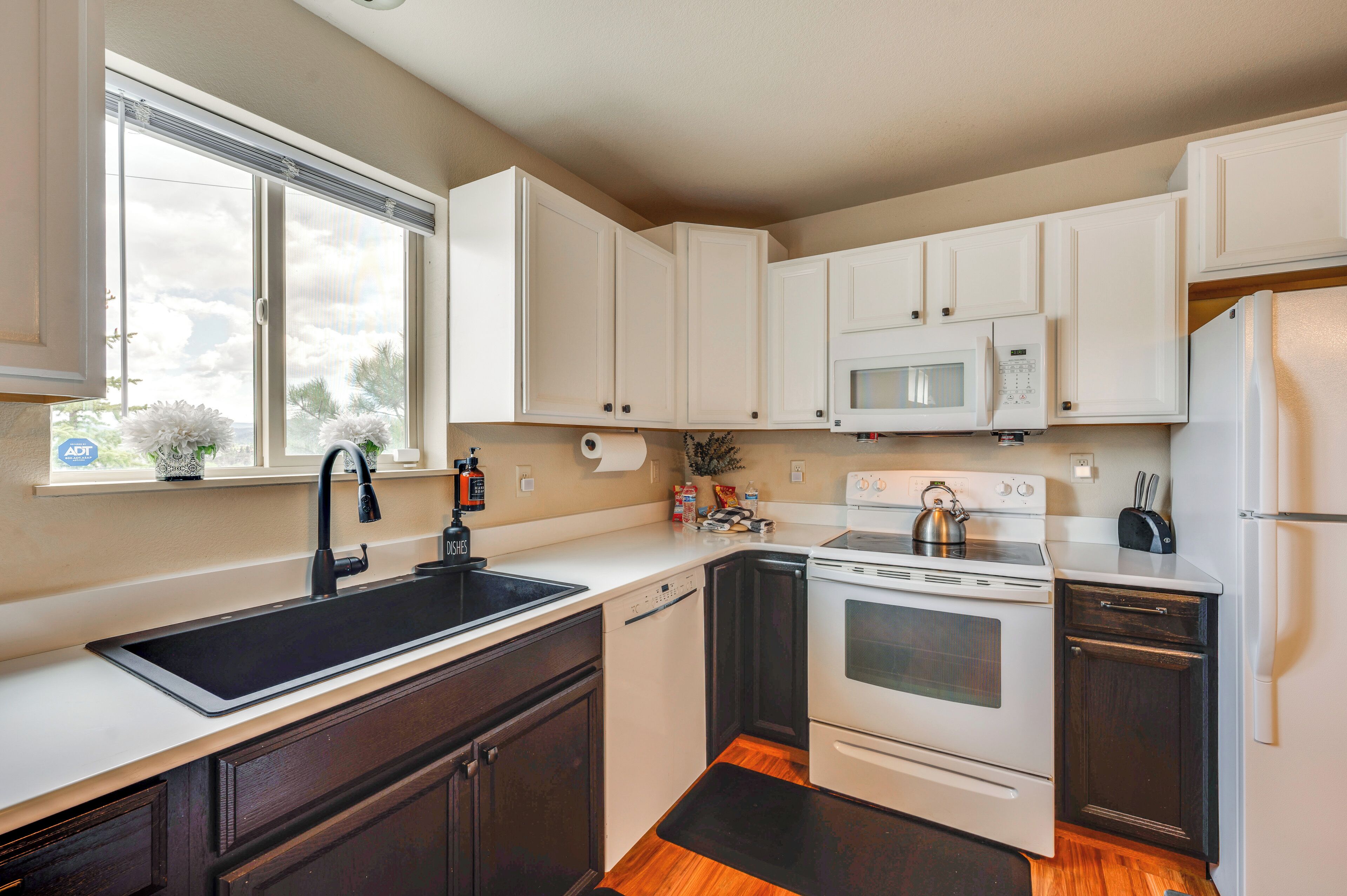 A compact kitchen with white cabinets, a black sink, a microwave, a stove, and a refrigerator.