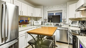 Une cuisine moderne avec des armoires blanches, des appareils en acier inoxydable, une table en bois et un four encastré.