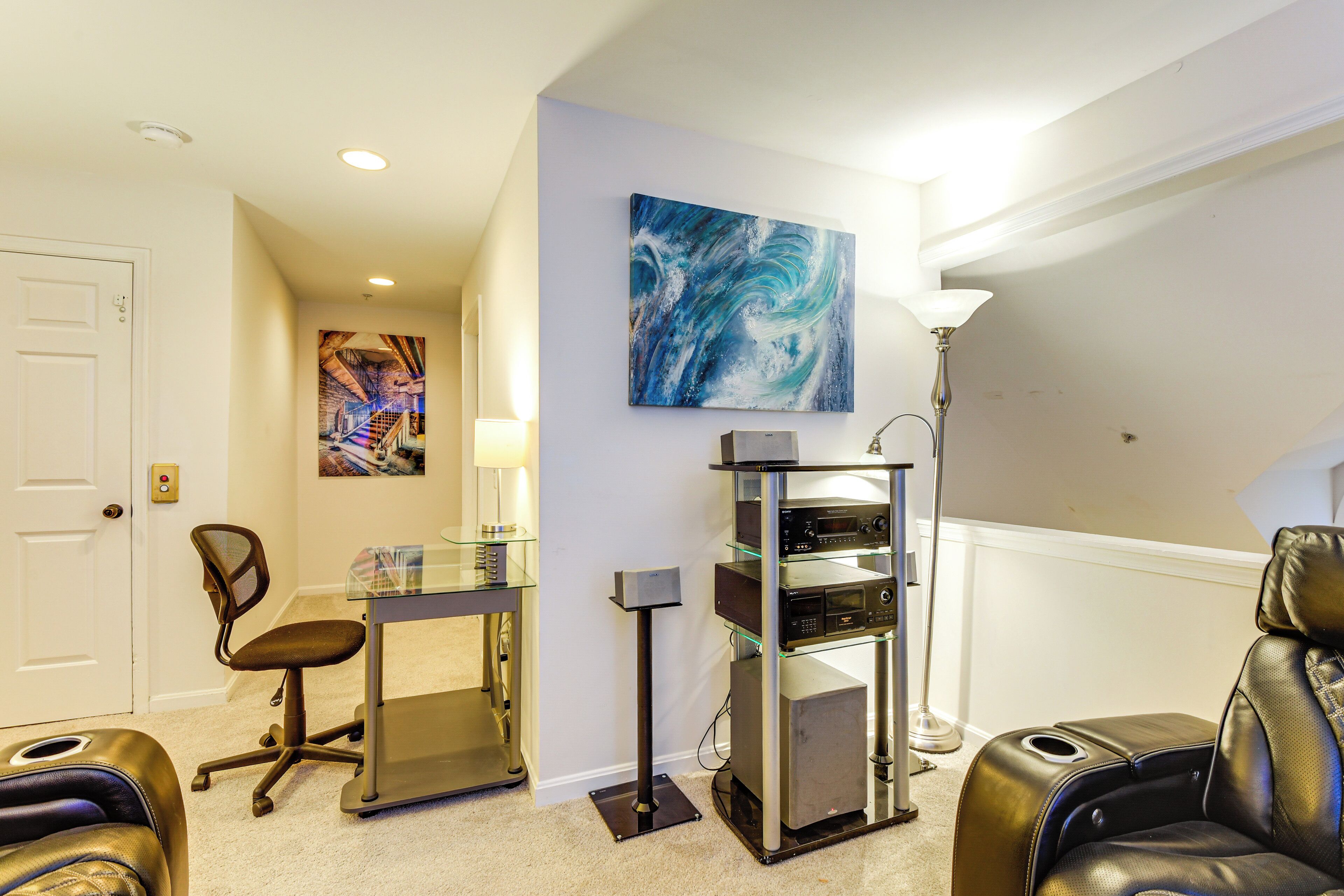 A room with a massage chair, a desk with a computer, a glass cabinet, and a painting on the wall.