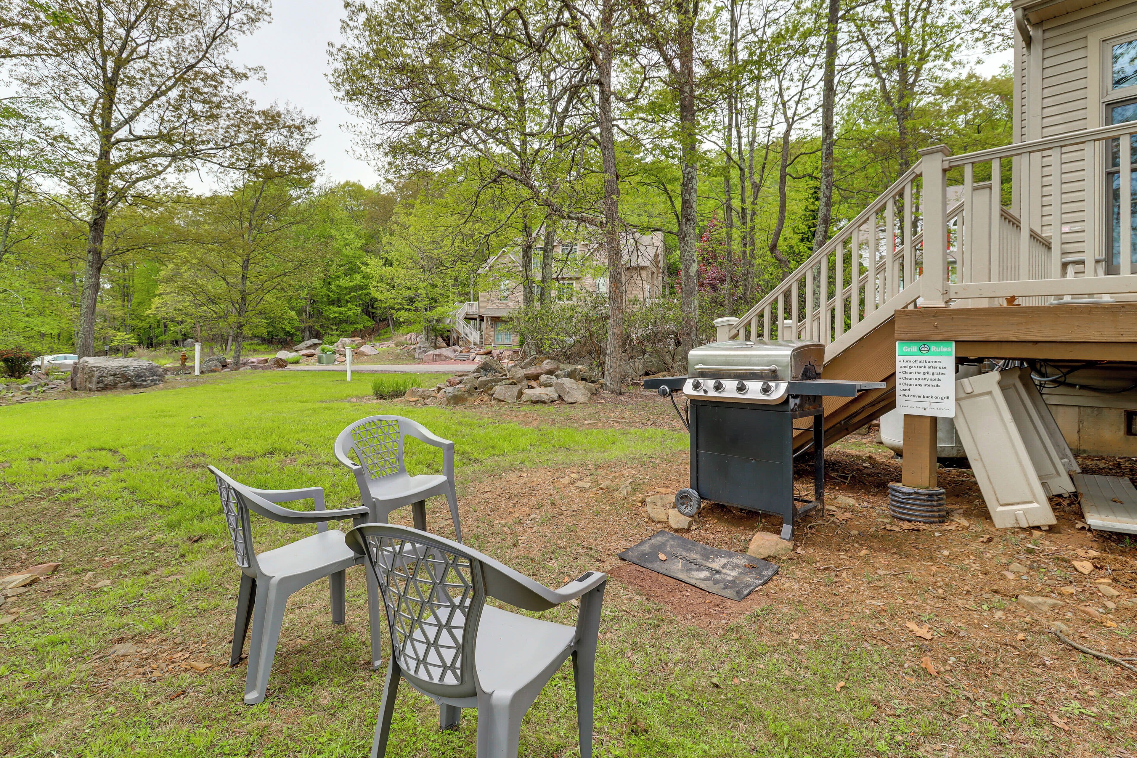 A backyard with a grill, two chairs, and a wooden deck.