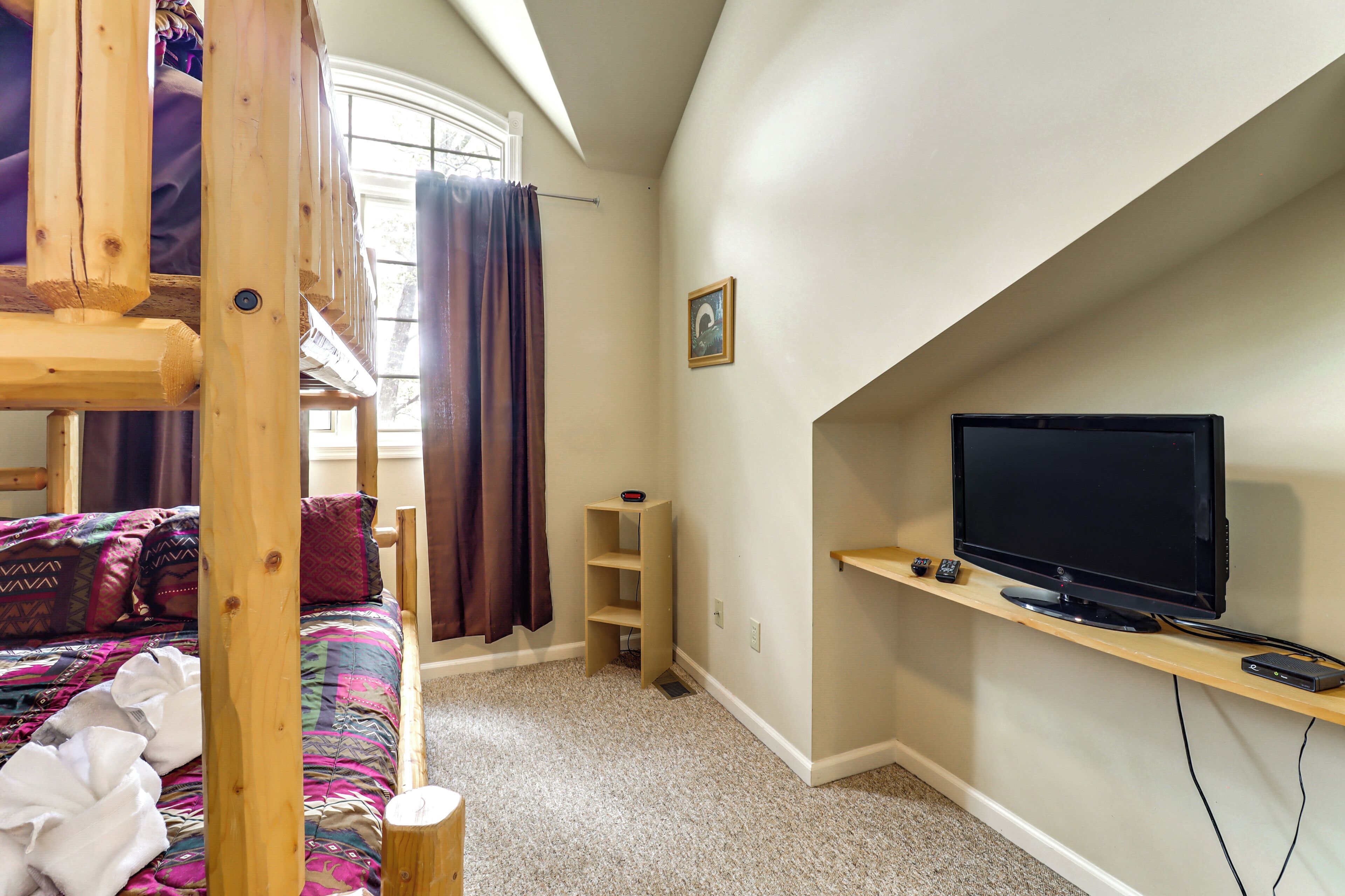 Une chambre avec un lit superposé, un téléviseur posé sur une étagère et une fenêtre avec des rideaux.