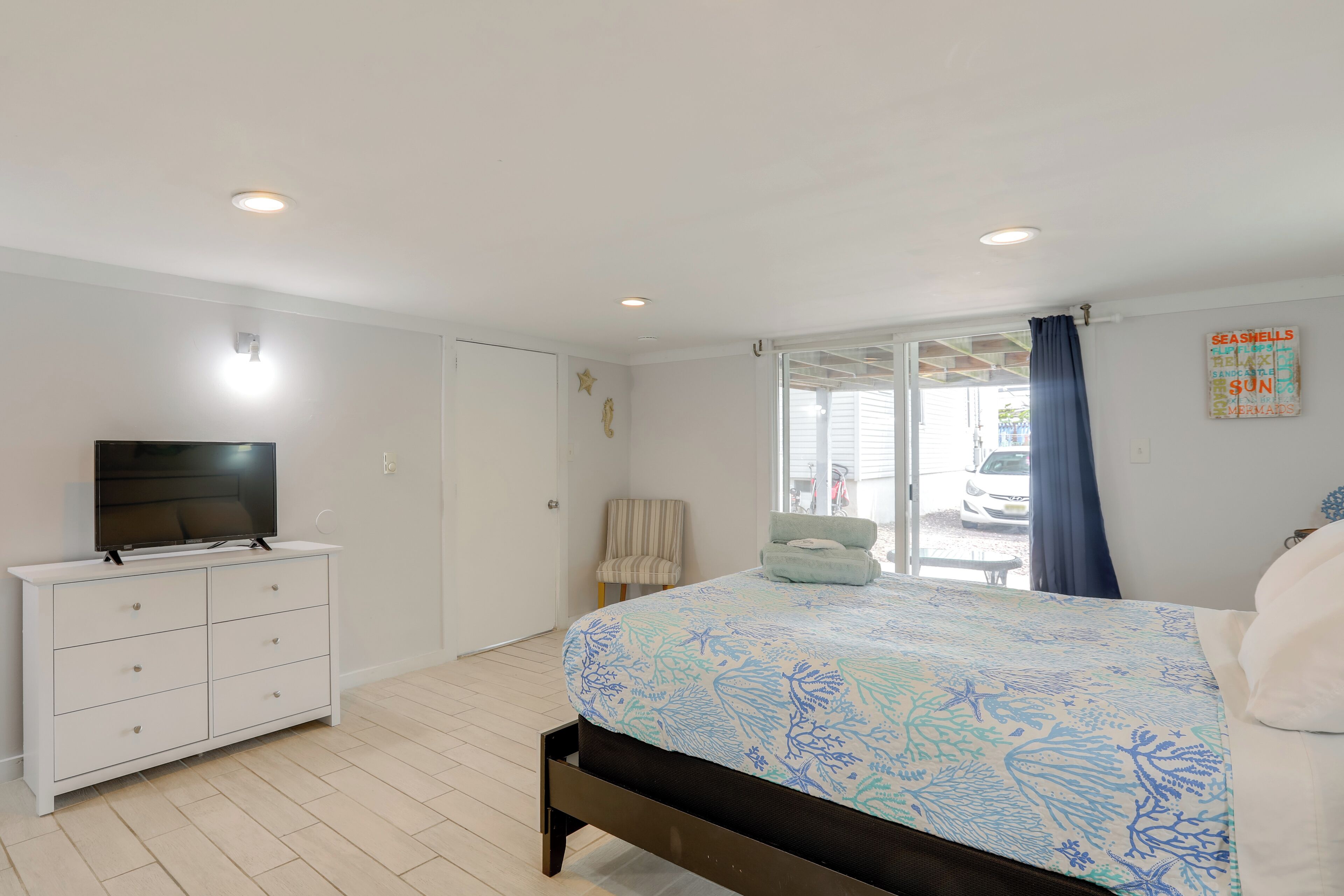 Een slaapkamer met een bed, een televisie op een dressoir, een stoel en een raam met gordijnen.