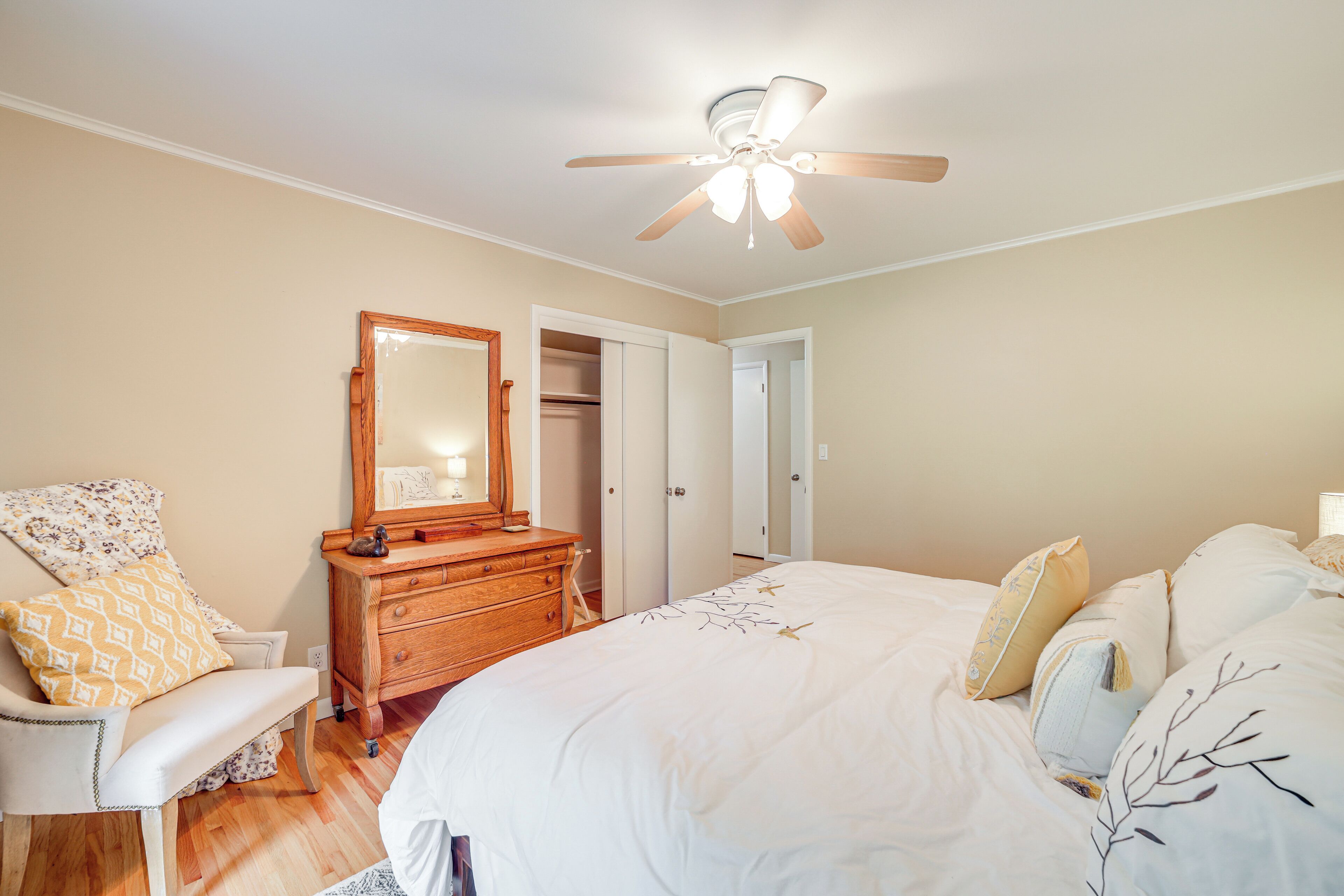 Un dormitorio con cama, cómoda, silla, ventilador de techo y puerta.