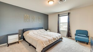 Ein Schlafzimmer mit einem Bett, einem Nachttisch, einem Stuhl und einem Fenster mit Vorhängen.