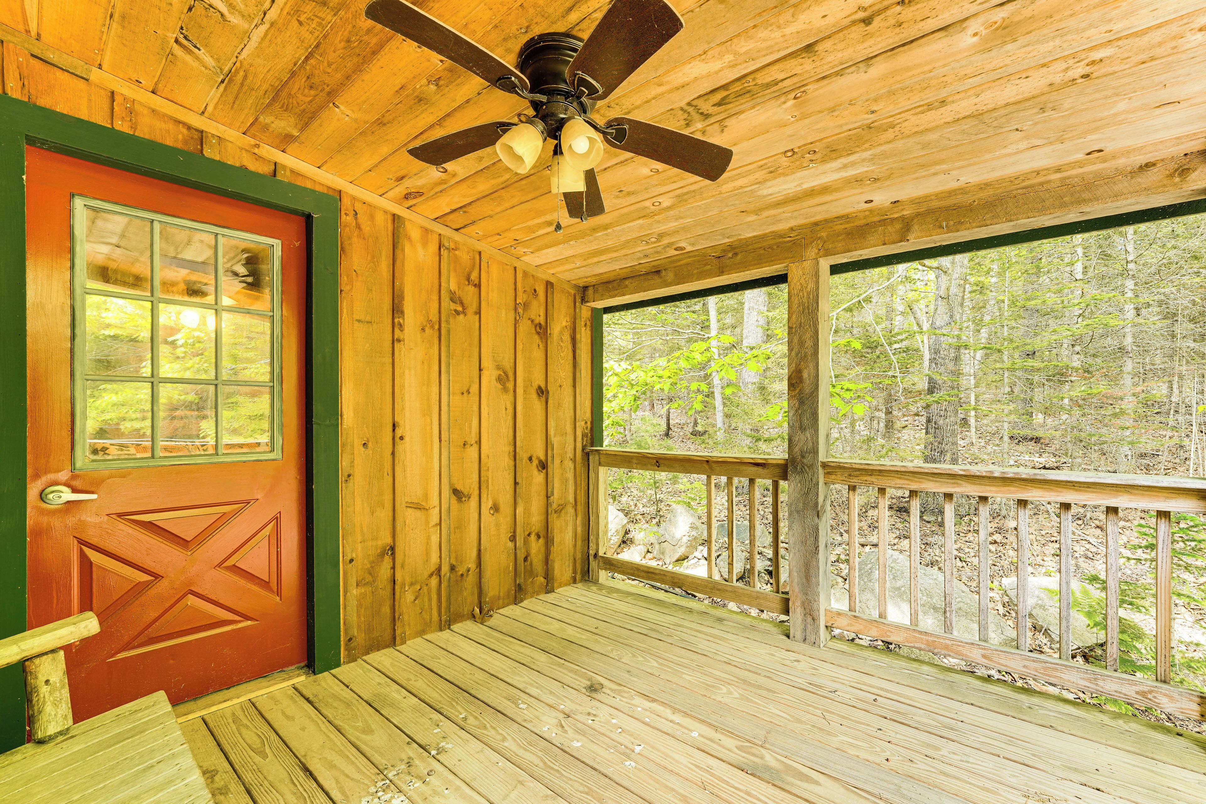 Une cabane en bois avec une porte rouge, un ventilateur de plafond et une grande fenêtre donnant sur une forêt.