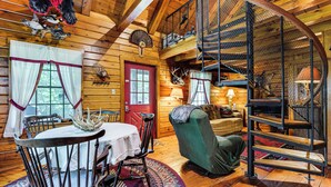 A cozy cabin interior with a dining area, a green armchair, a staircase, and a red door. - 35 Mi to Acadia: Rustic Retreat in Orland! (Orland)