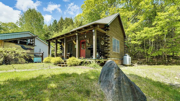 A rustic log cabin with a porch, surrounded by lush greenery and trees. - 35 Mi to Acadia: Rustic Retreat in Orland! (Orland)