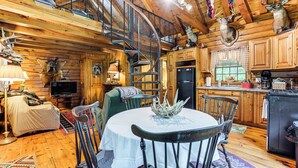 A rustic cabin interior with a dining table, chairs, a spiral staircase, wooden walls, and mounted animal heads. - 35 Mi to Acadia: Rustic Retreat in Orland! (Orland)