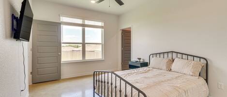 A bedroom with a bed, a ceiling fan, a window, and a door.