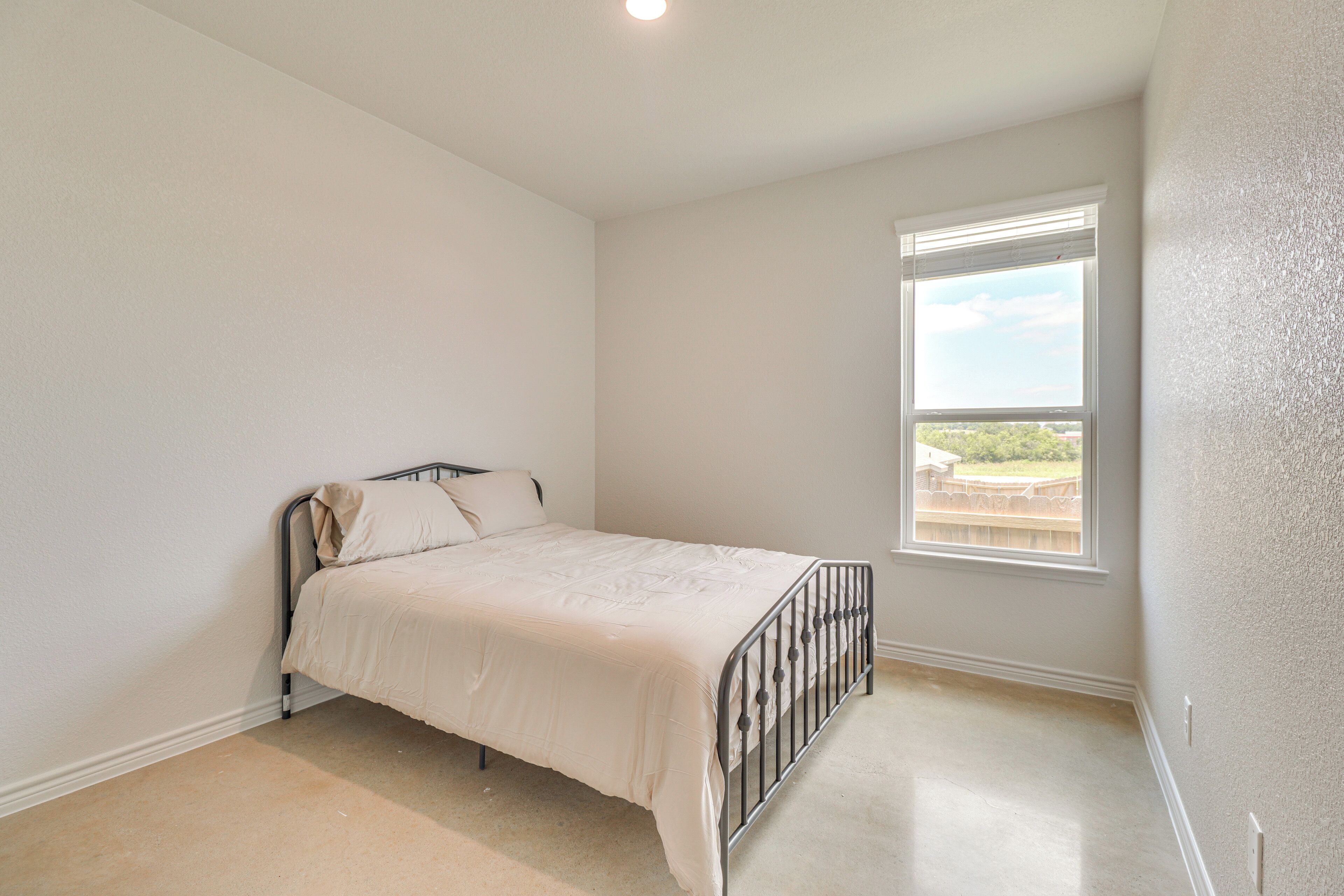 A bedroom with a single bed, a window with blinds, and a view of greenery outside.