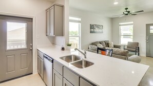 A modern kitchen with a large island, stainless steel appliances, and a dining area with a gray sofa and a chair. - 2 Mi to Dtwn Dining! Pet-friendly Temple Townhome (Temple)