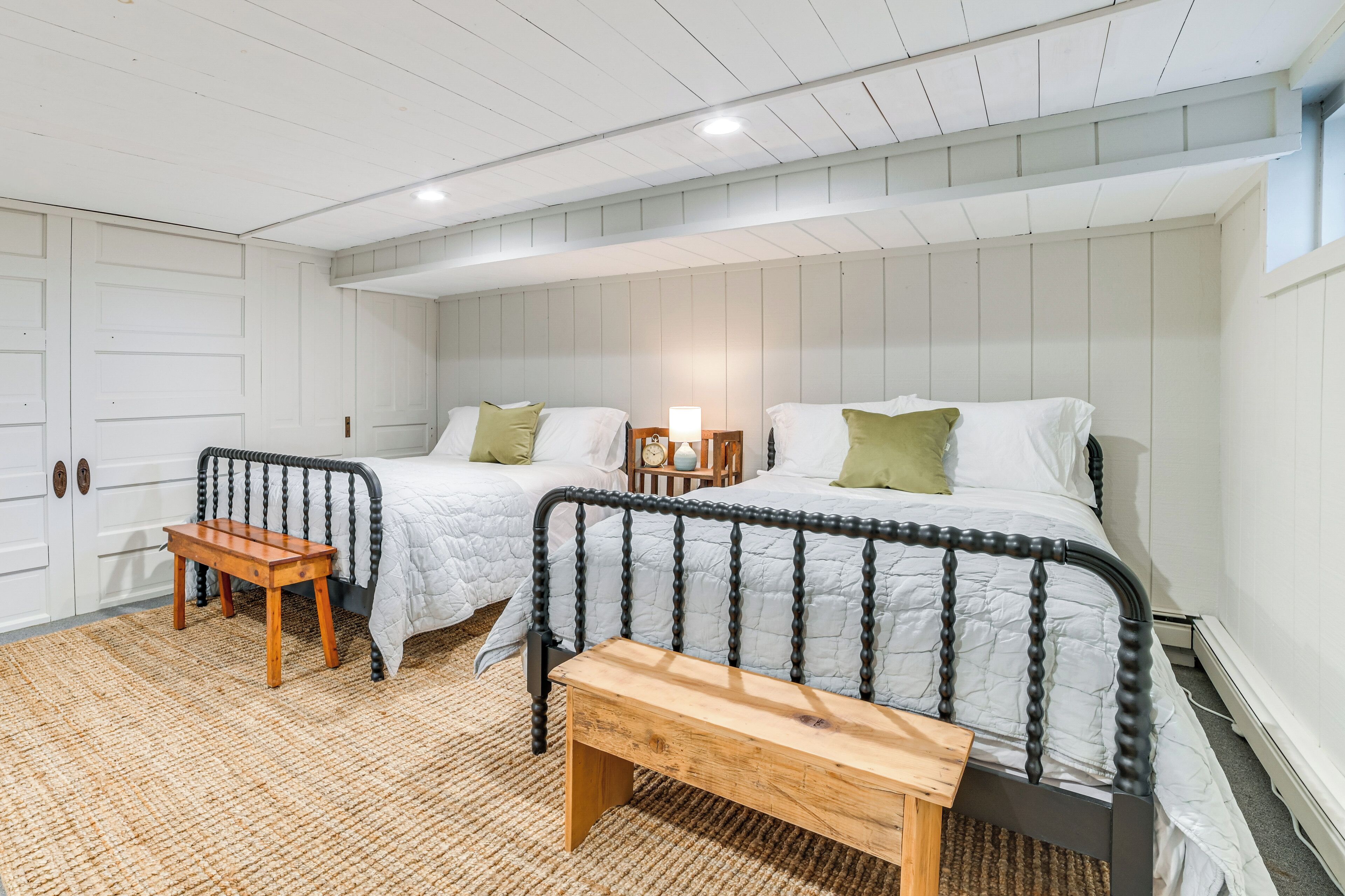 Un dormitorio con dos camas, un banco de madera, una mesita pequeña y una mesita de noche con lámpara.