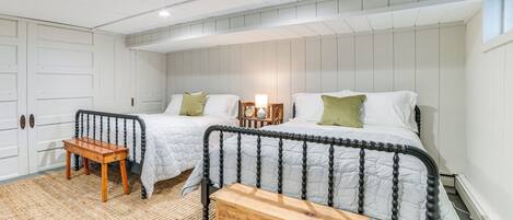 Un dormitorio con dos camas, un banco de madera, una mesita pequeña y una mesita de noche con lámpara.
