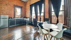 Eine Küche mit Backsteinwand, Kühlschrank und Spüle. Zwei weiße Stühle und ein Tisch sind ebenfalls vorhanden.
